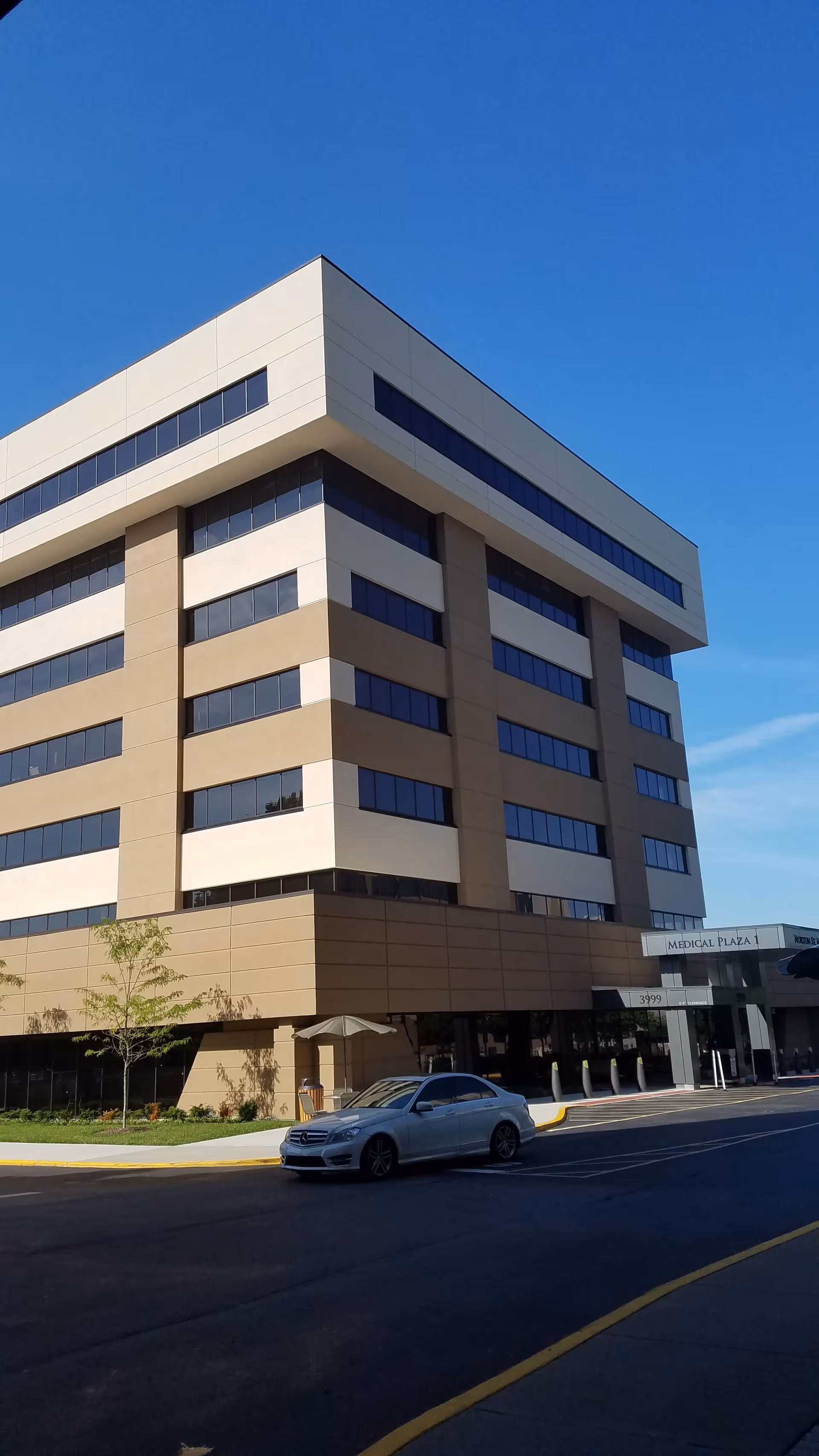 Exterior view of a tall beige medical plaza building with blue windows and streetfront.