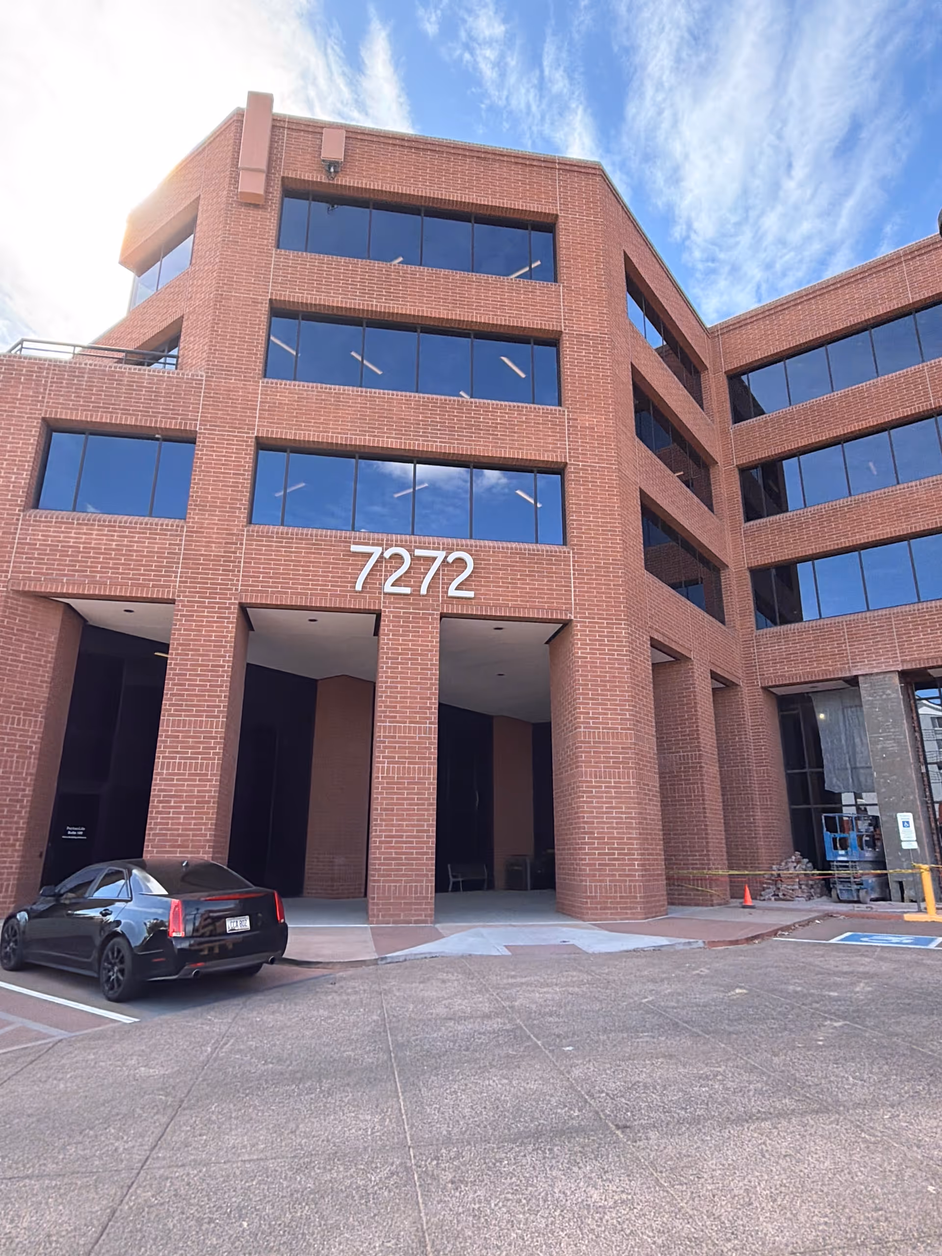 Brick multi-story building with large windows, address 7272, and a parked black car.