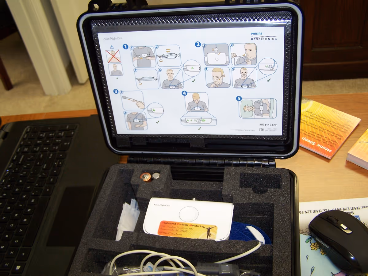 Open case shows portable monitoring device, instruction card, and cables on a desk.