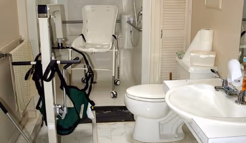 Accessible bathroom with toilet, sink, shower chair, and mobility equipment.