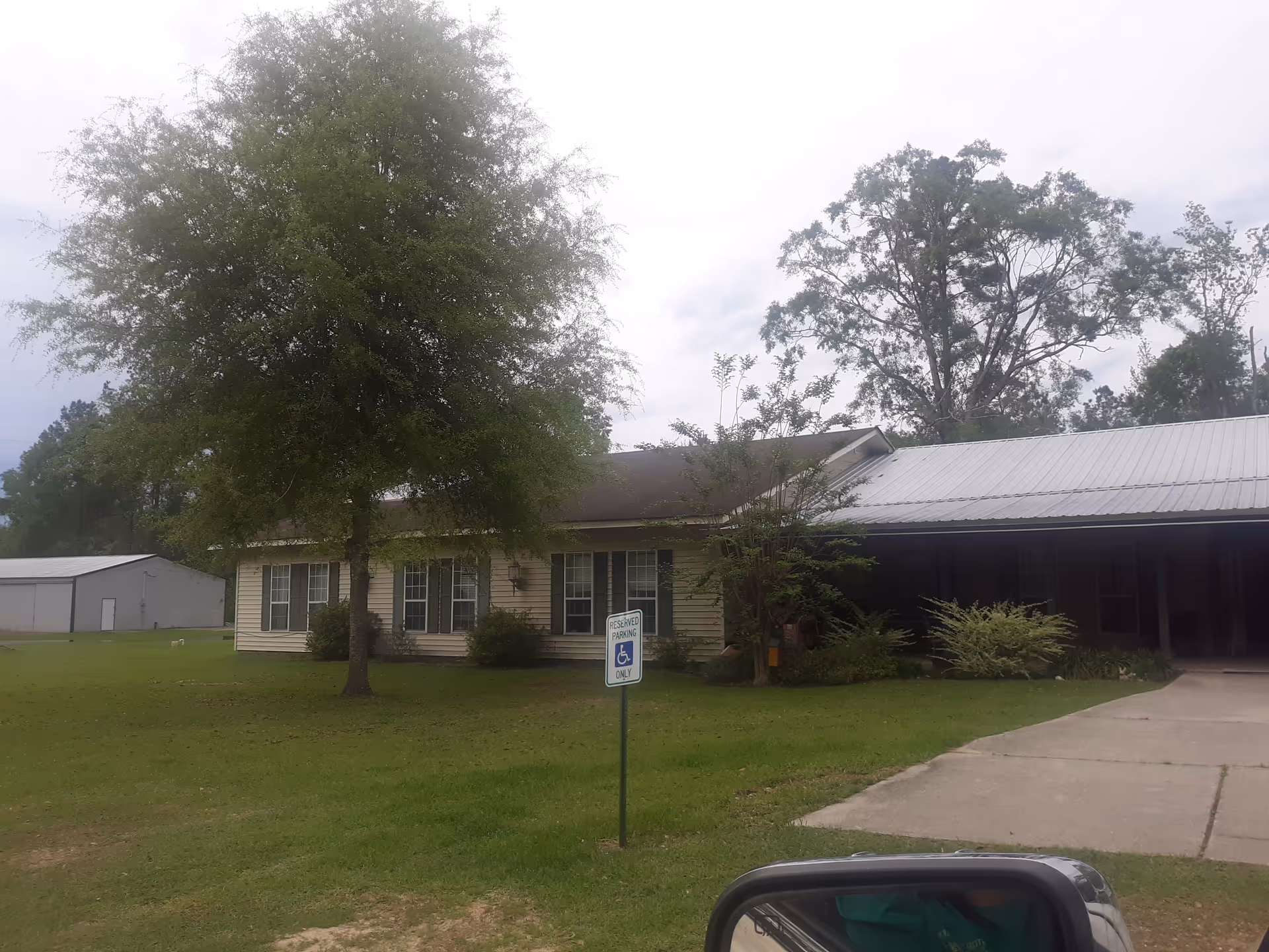 Front exterior of a single-story senior living building with trees and a handicap parking sign.