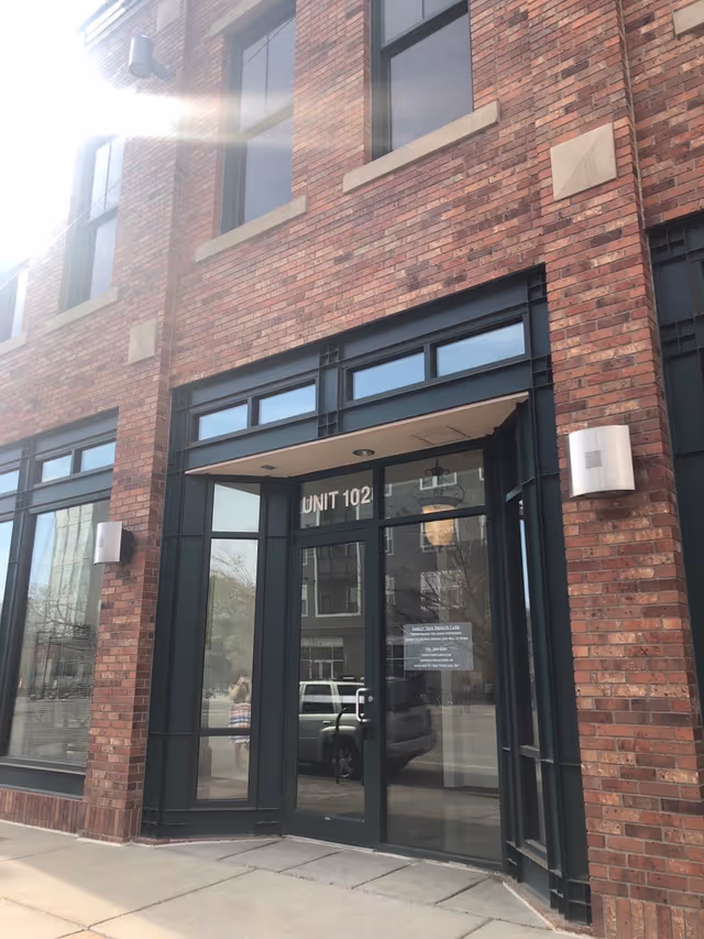 Brick building entrance labeled Unit 102 with glass doors and windows.