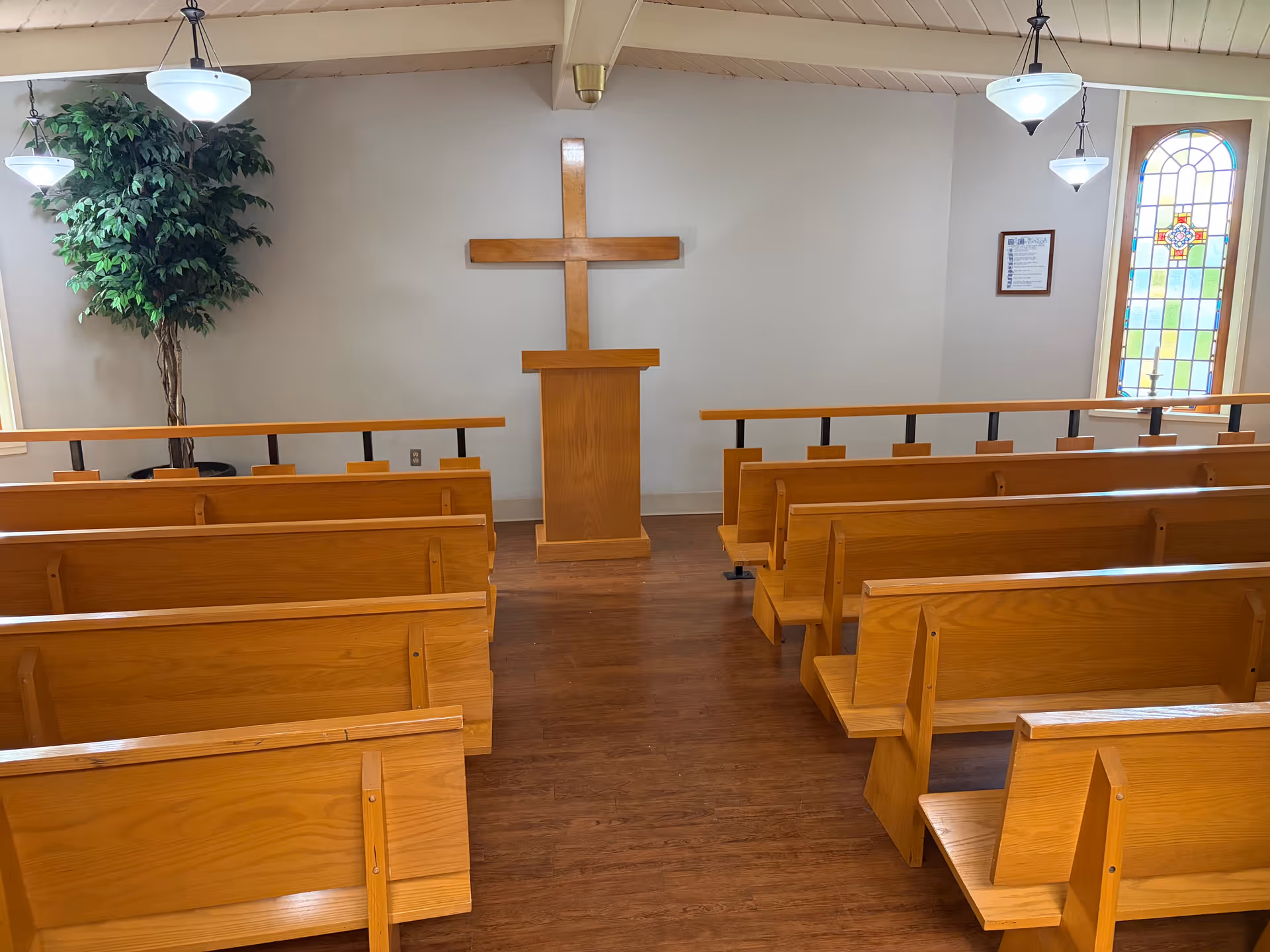 Wooden pews face a central pulpit in a small chapel with a cross.