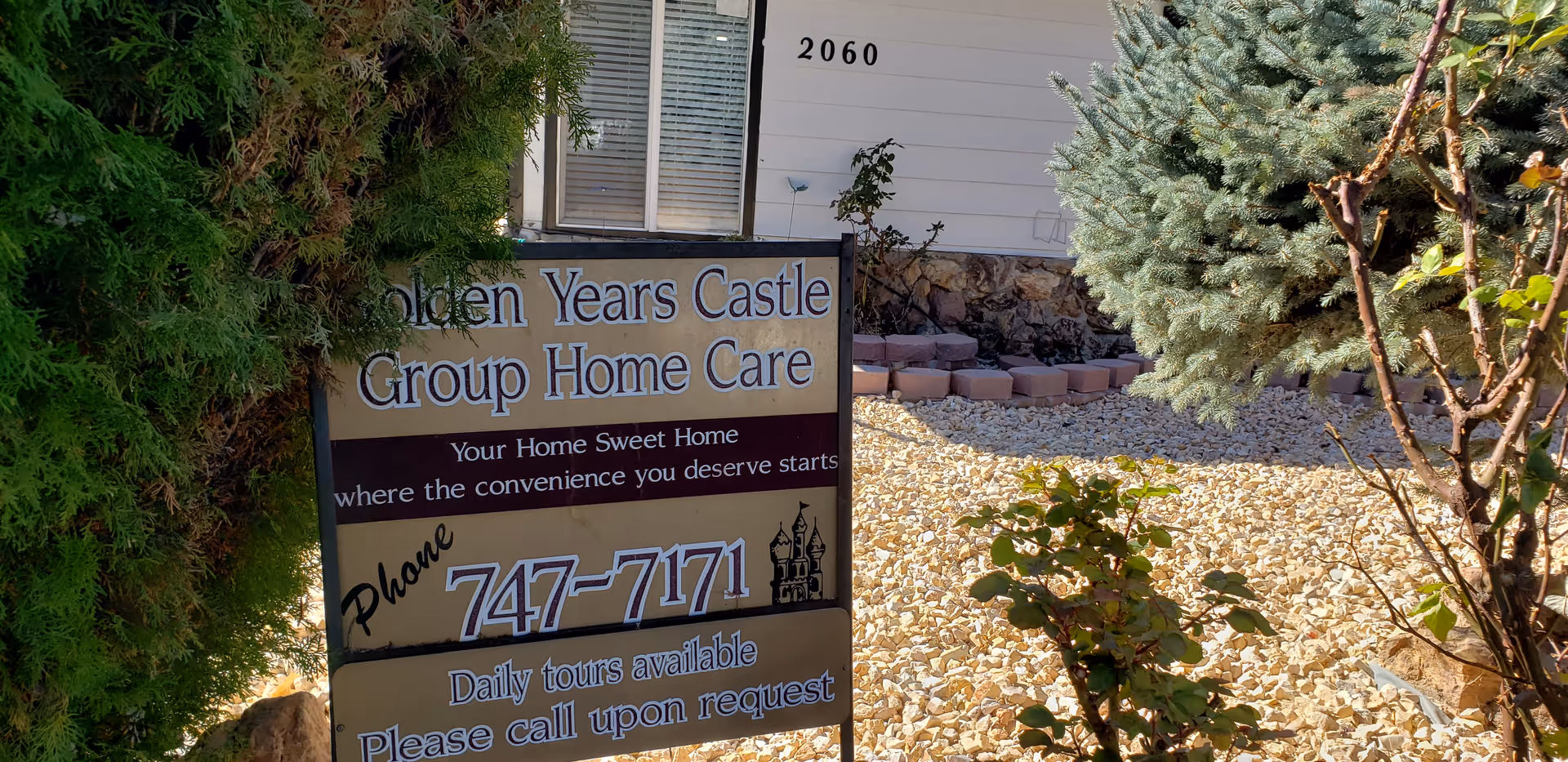 Exterior view of a sign for Golden Years Castle Group Home Care in a gravel yard.