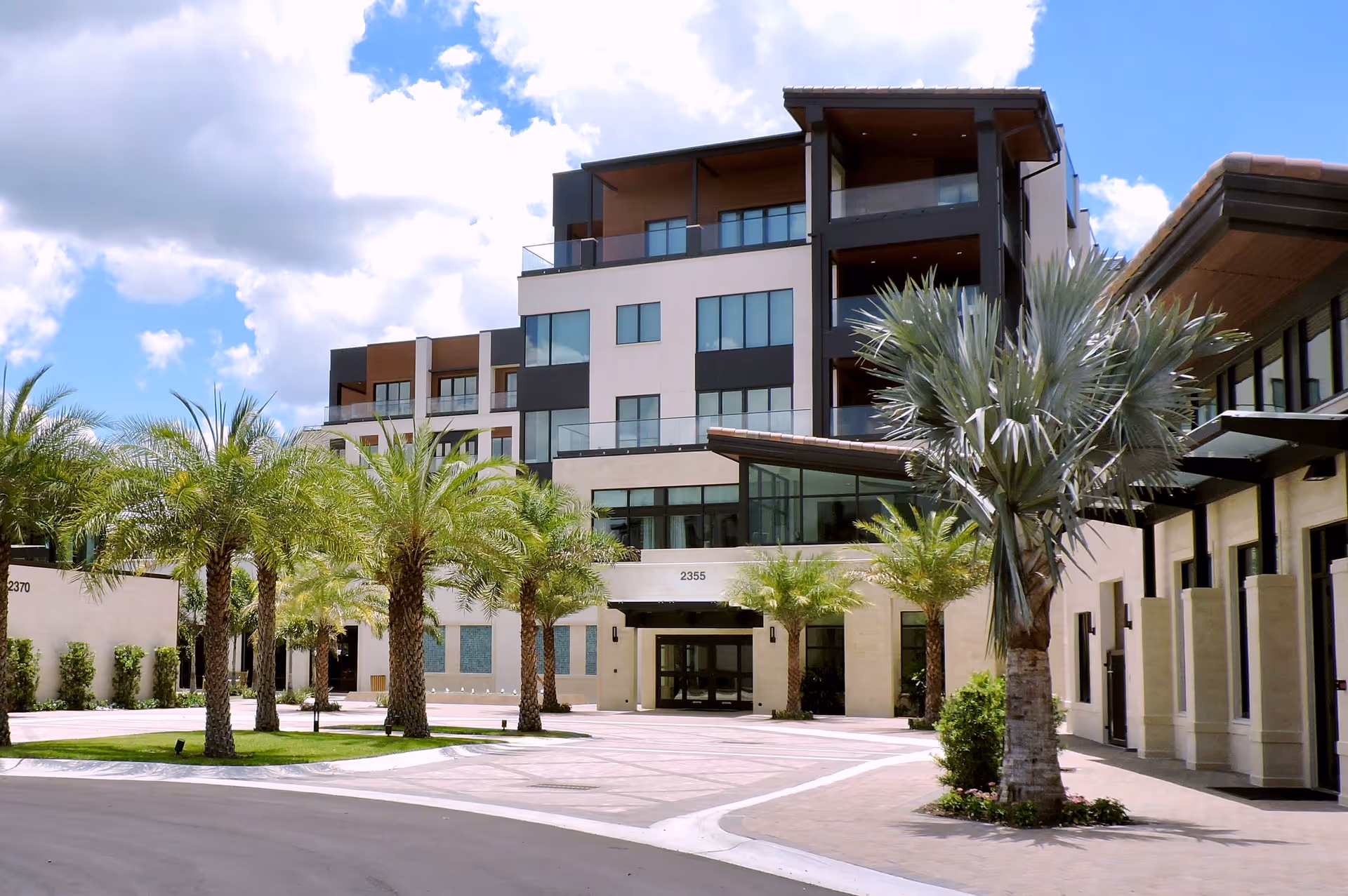 Exterior of Moorings Park at Grey Oaks: modern multi-story building with palm trees and a driveway.