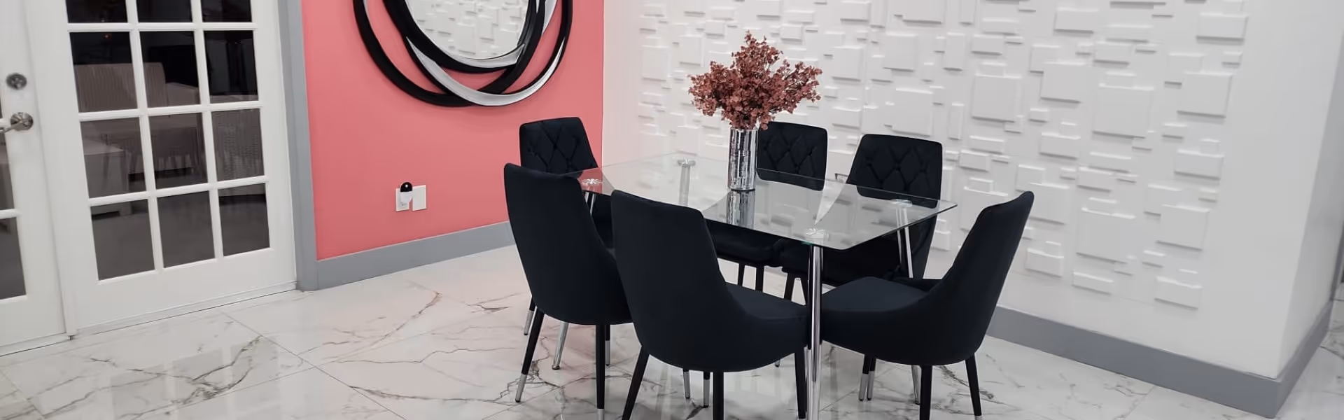 A modern dining area with a glass table and black chairs, featuring pink walls and decorative elements.