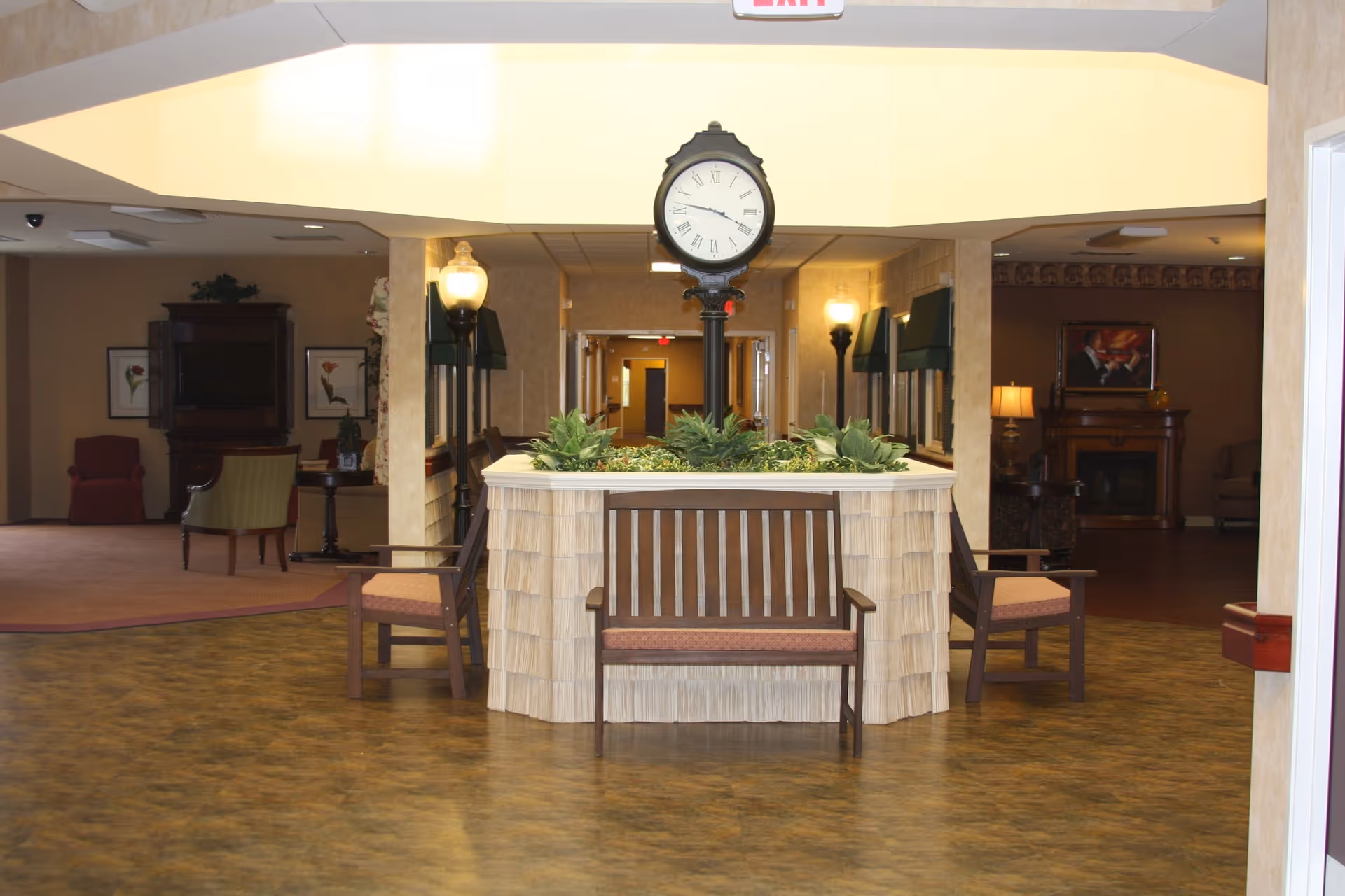 Interior common lobby area with a central planter topped by a tall clock and benches, with seating and lamps in the background.