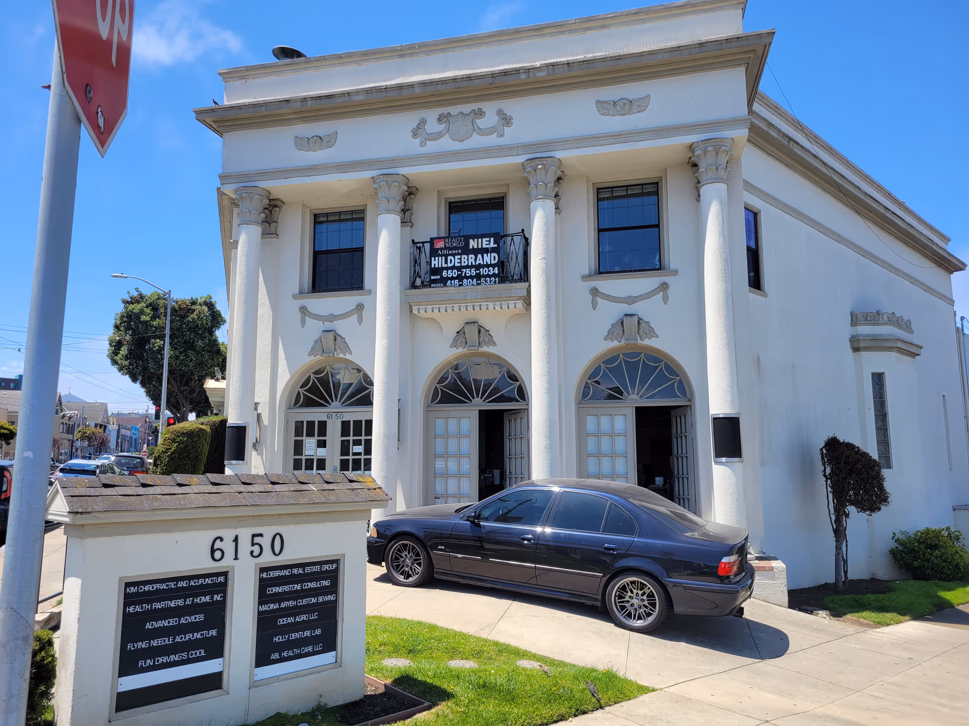 White two-story building with columns and a black car parked in front.