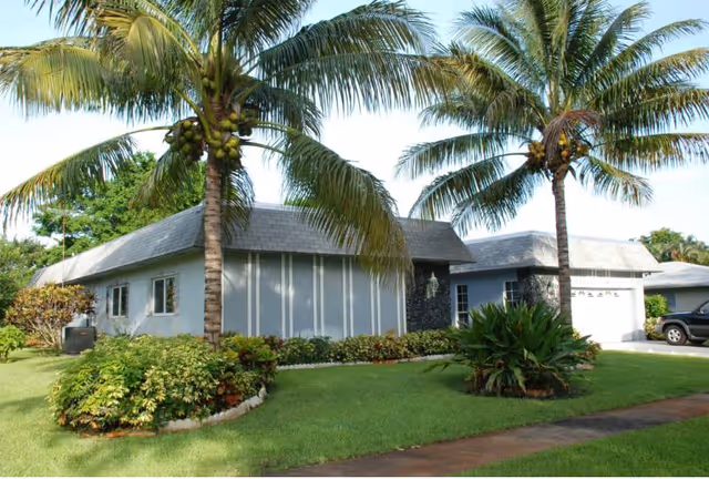 Single-story senior living facility with palm trees and a neatly landscaped front lawn.