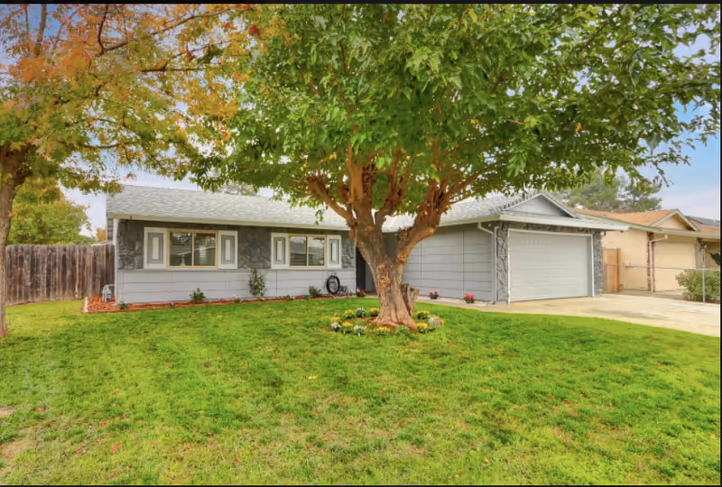 Single-story gray ranch-style house with a large tree and green lawn in front yard.