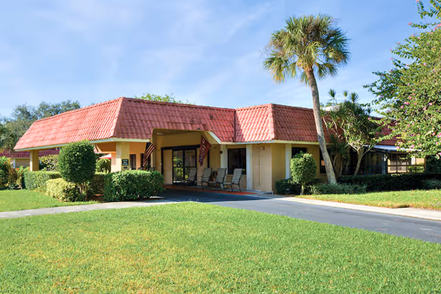 Exterior view of a Brookdale senior living building with a red-tiled roof and palm trees.