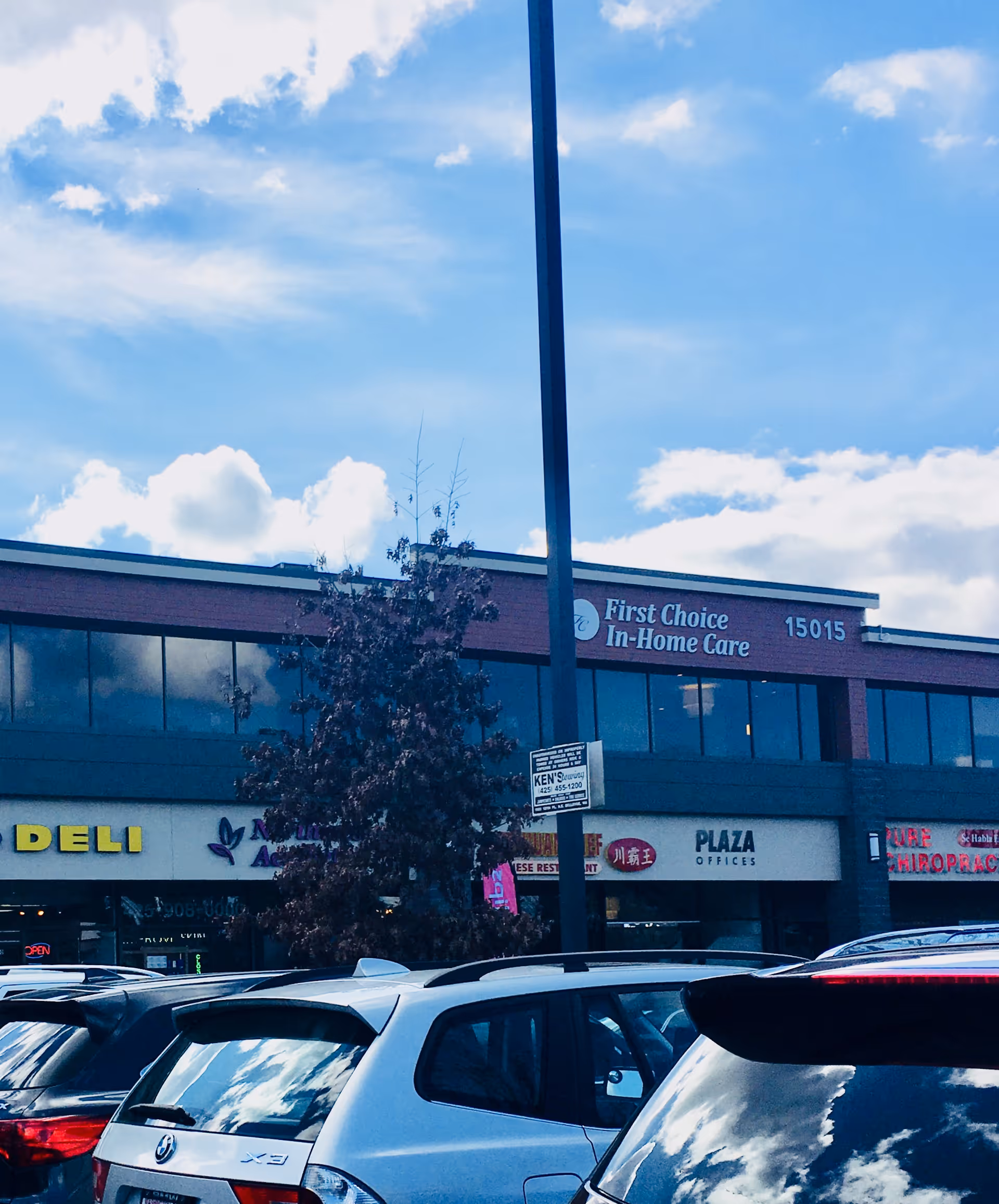 Exterior view of a shopping plaza with First Choice In-Home Care sign and parked cars.