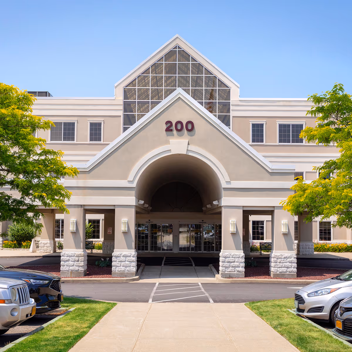Front view of a beige medical building with an arched entrance and a parking lot.