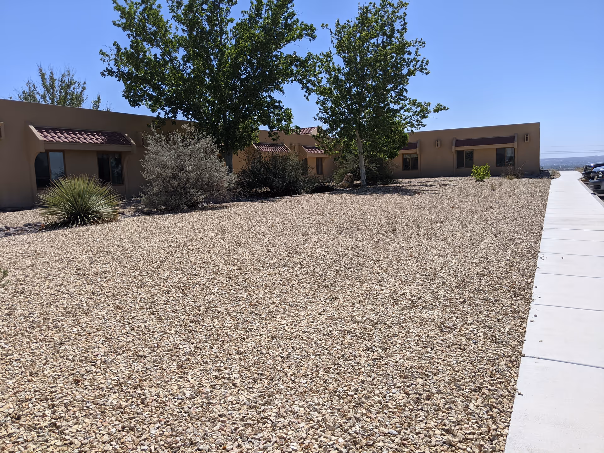 Single-story beige facility exterior with gravel yard, trees, and a concrete sidewalk.