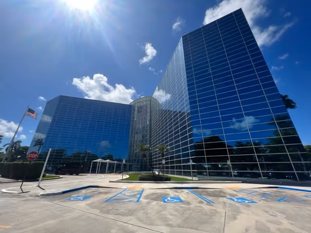 Modern glass-front building with blue sky, parking lot, and accessible parking spots.