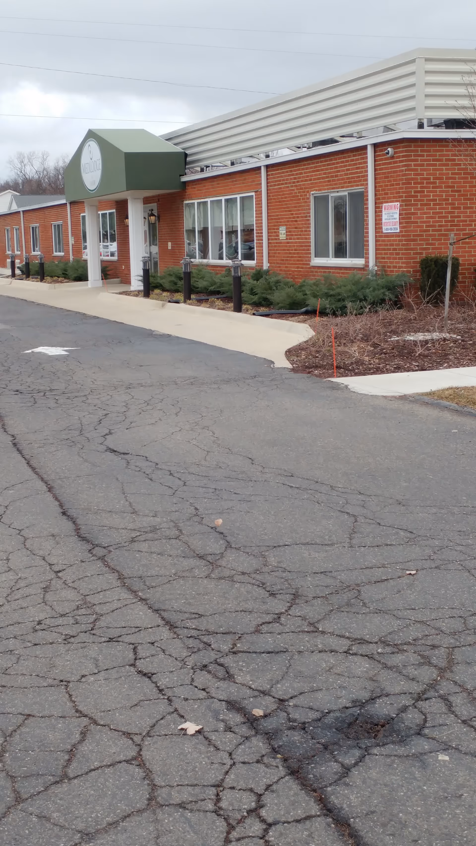 Medilodge of Taylor exterior: red brick building with green awning entrance, in a cracked parking lot.