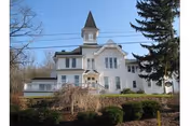 A white multi-story building with a central tower, front yard shrubs, and leafless trees.