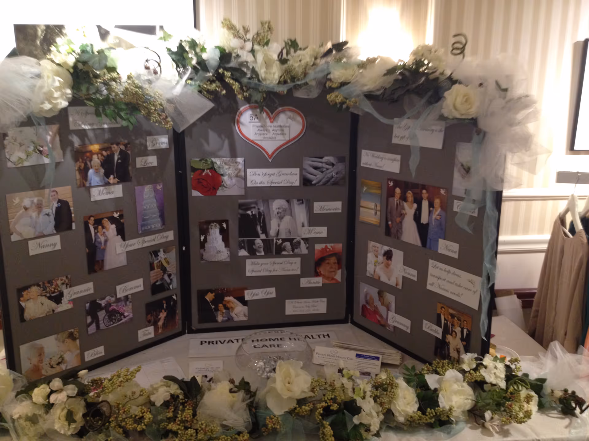 Decorative photo board with flowers and photos displayed on a table in an indoor setting.