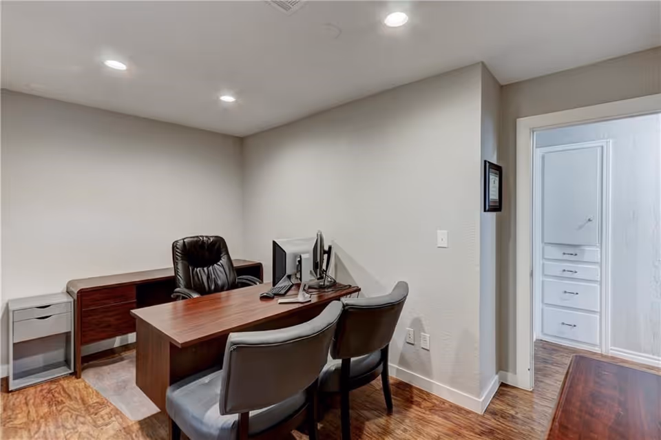A small, organized office with desk, two chairs, computer, and filing cabinets.