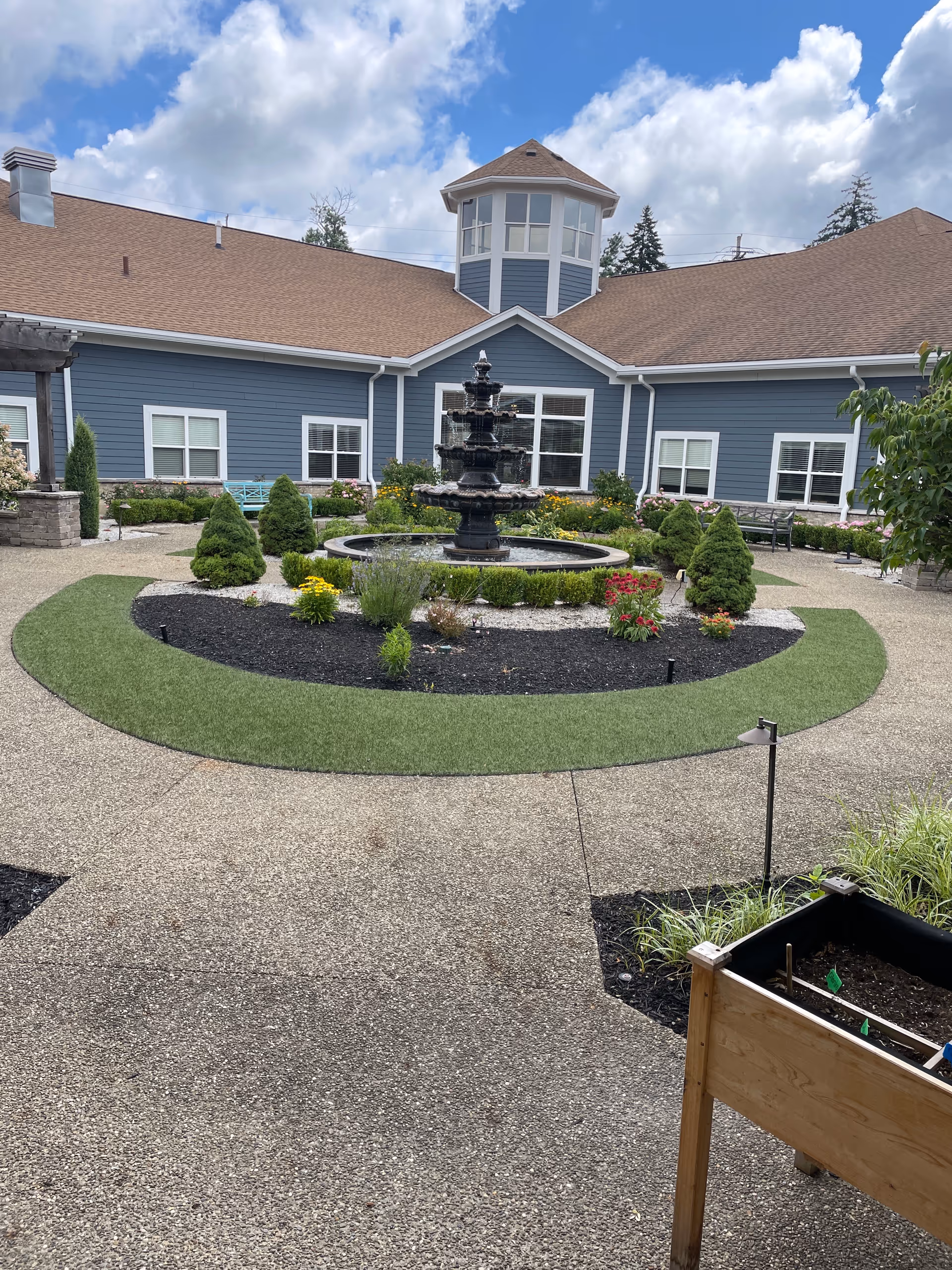 Blue senior living facility with circular fountain courtyard and landscaped gardens.