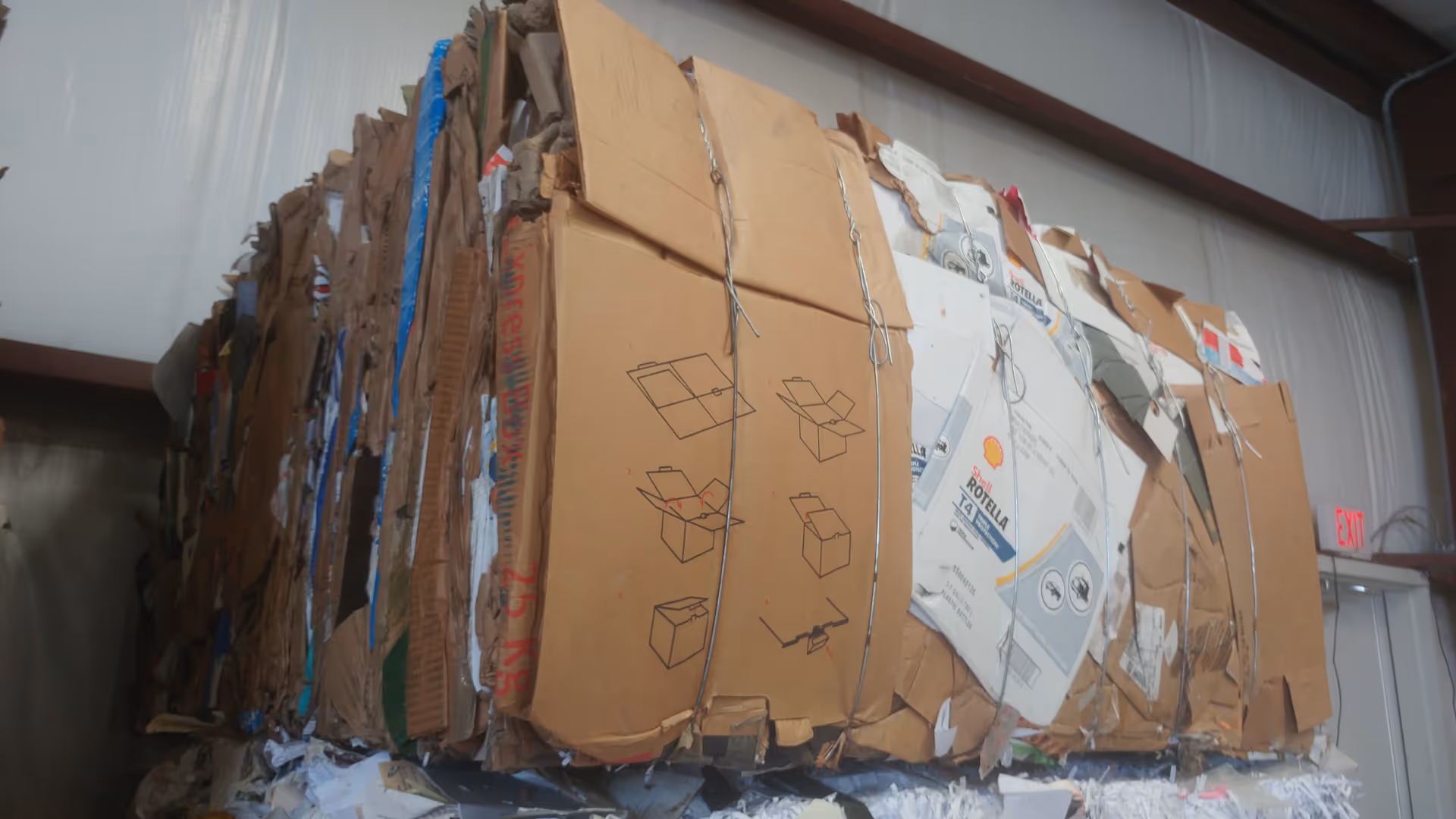 Inside a recycling facility, a towering pile of flattened cardboard boxes.