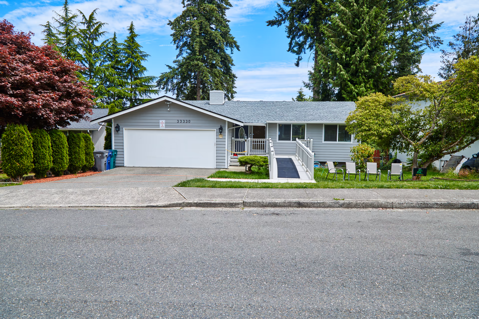 Single-story gray house with ramp access, a two-car garage, and lawn seating.