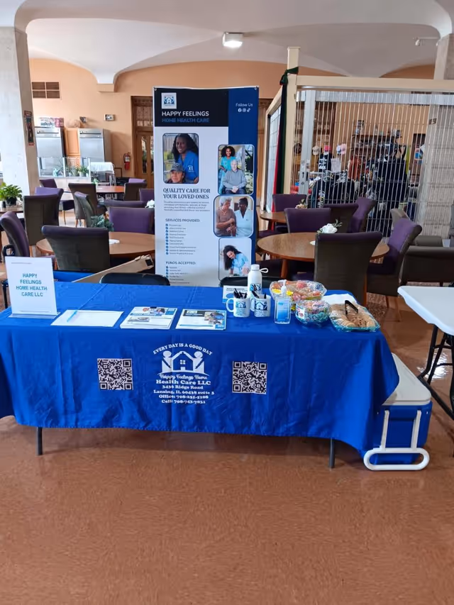 Promotional booth with blue tablecloth and banner for Happy Feelings Home Health Care inside a lounge.
