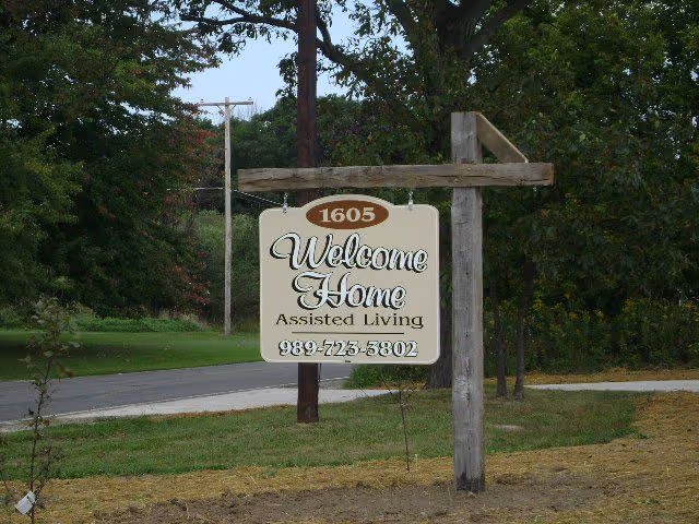 Wooden post sign reading Welcome Home Assisted Living beside a road.