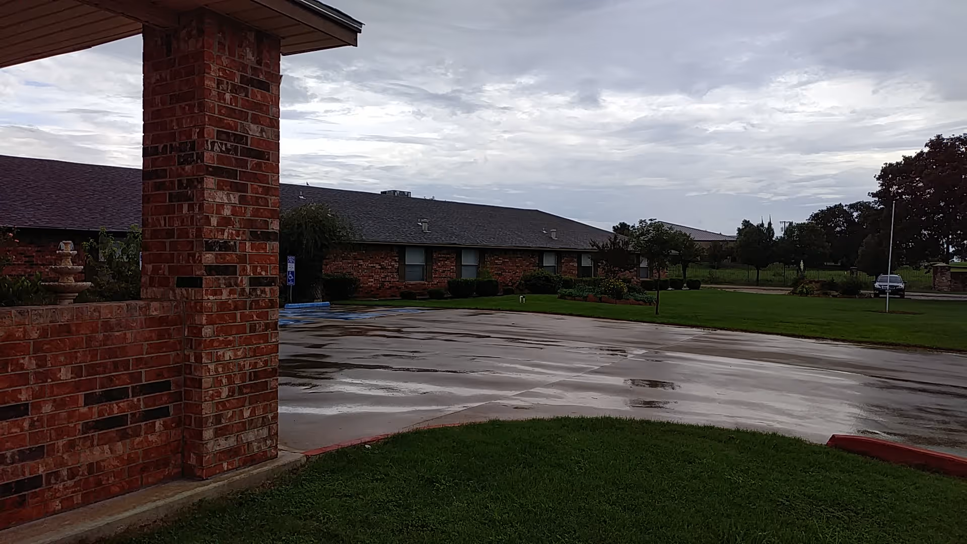 Exterior view of Songbird Lodge: brick building, wet parking lot, and grassy lawn.