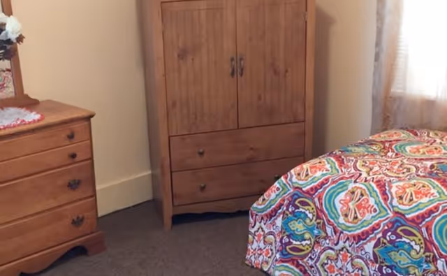 Wooden dresser and armoire beside a bed with a colorful quilt in a bedroom.