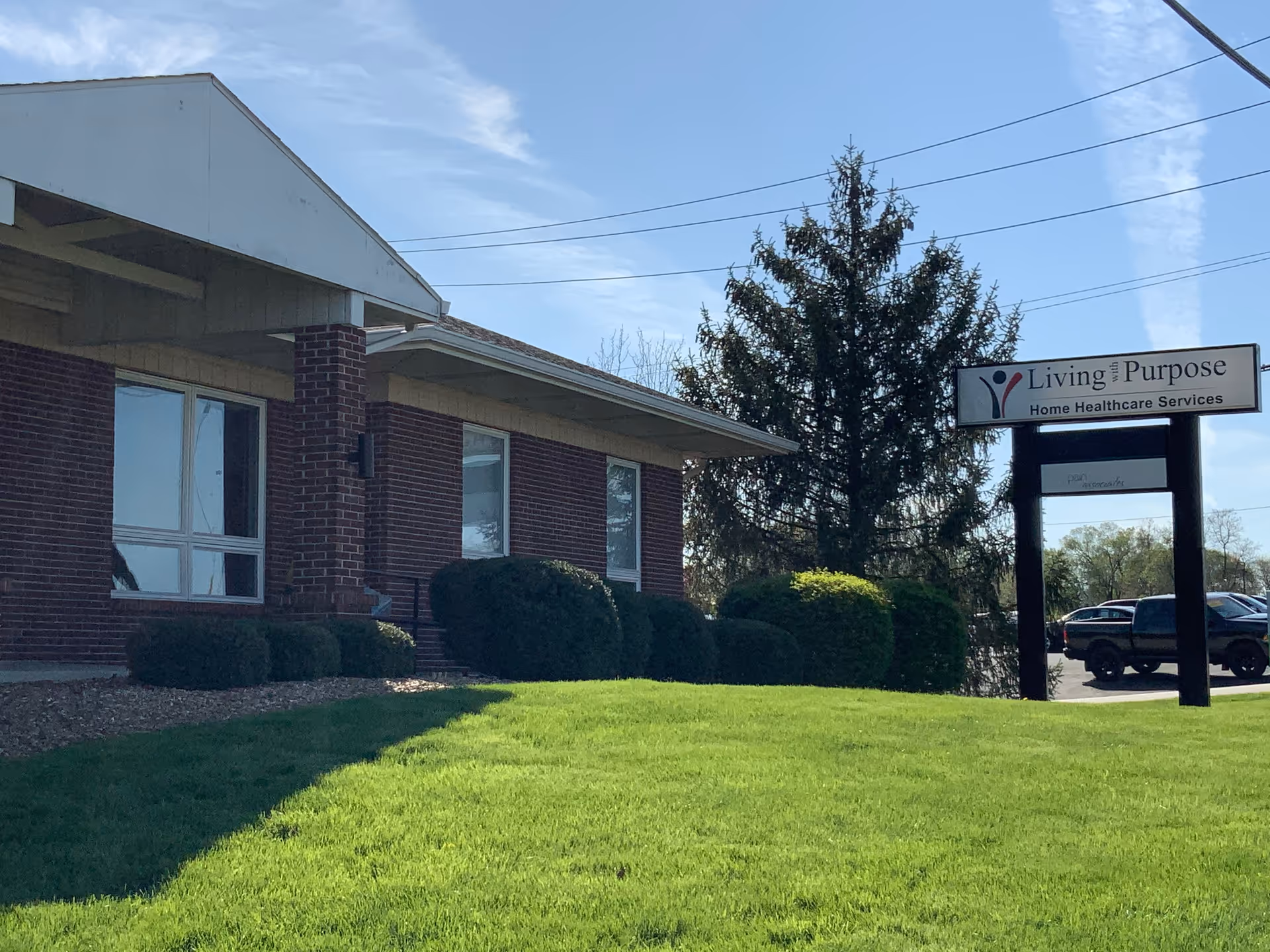 Brick building exterior with trimmed bushes and a sign advertising Living with Purpose Home Healthcare Services.