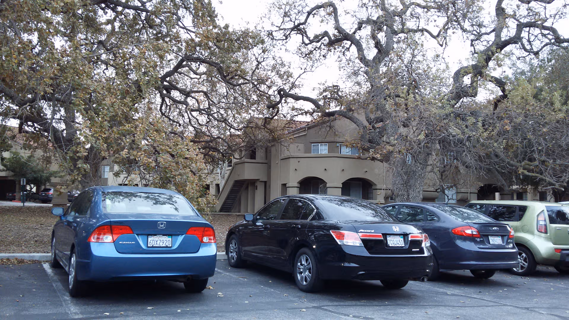 Exterior view of Atria Hillcrest with parked cars and a beige multi-story building under trees.