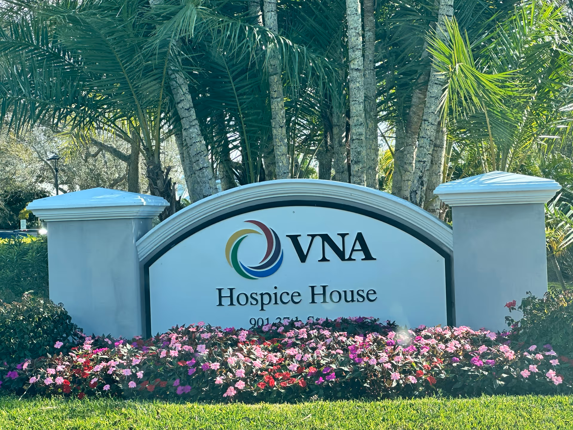 Front sign for VNA Hospice House with palm trees and flowers