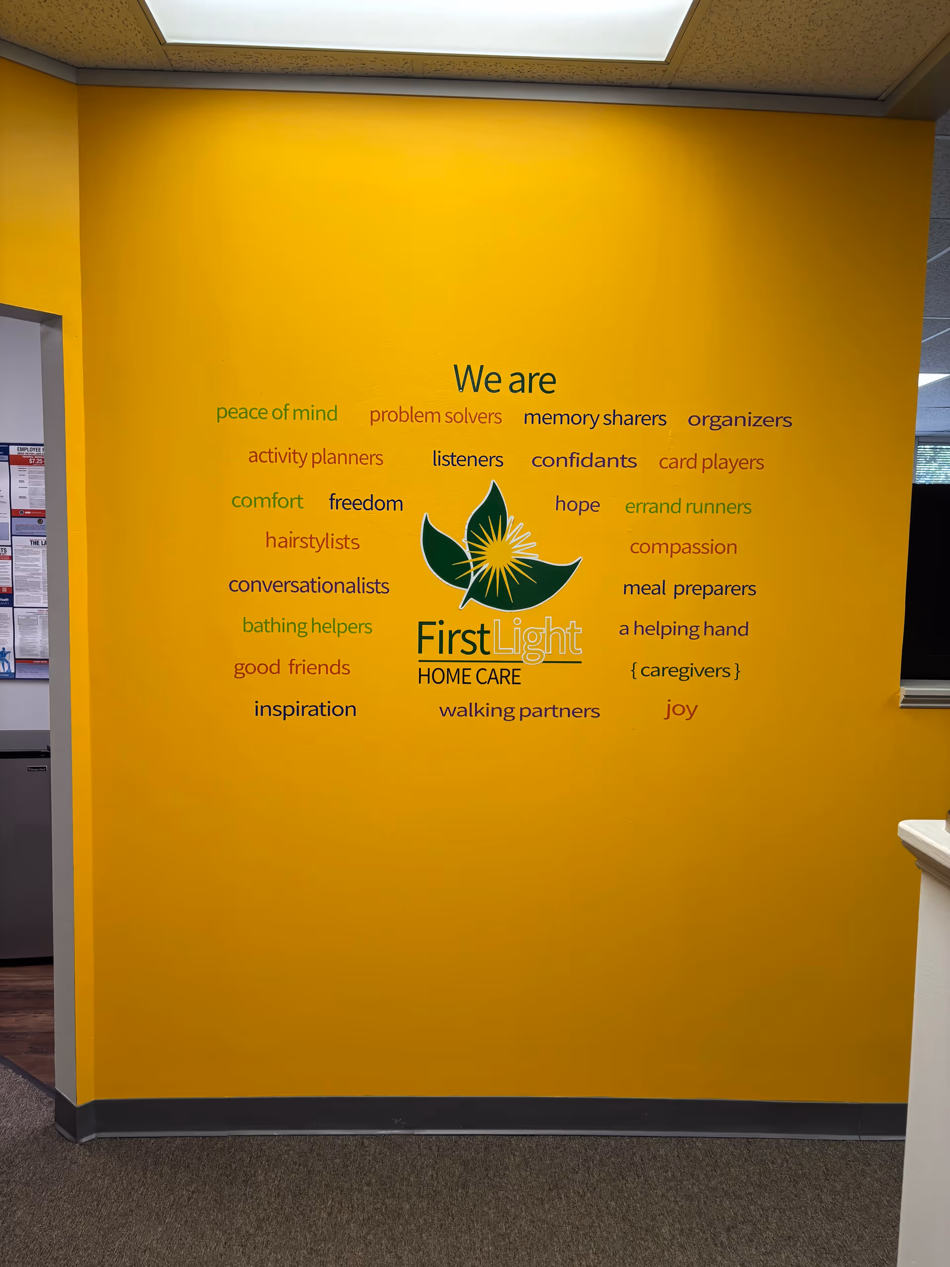 Bright yellow interior wall with FirstLight Home Care logo and the words We are.