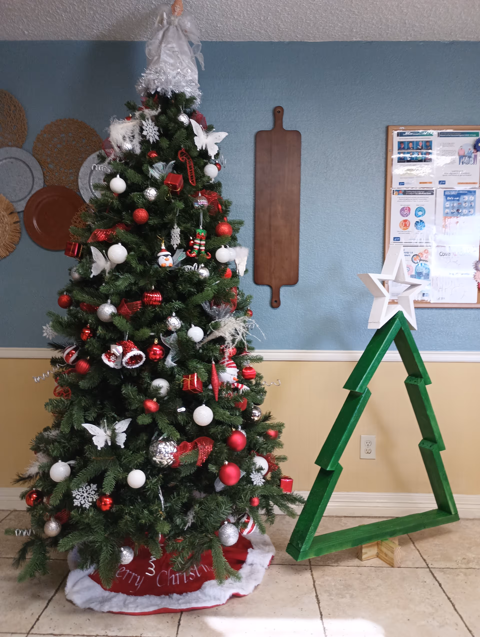 Decorated Christmas tree stands indoors beside a green star-shaped display in a community room.