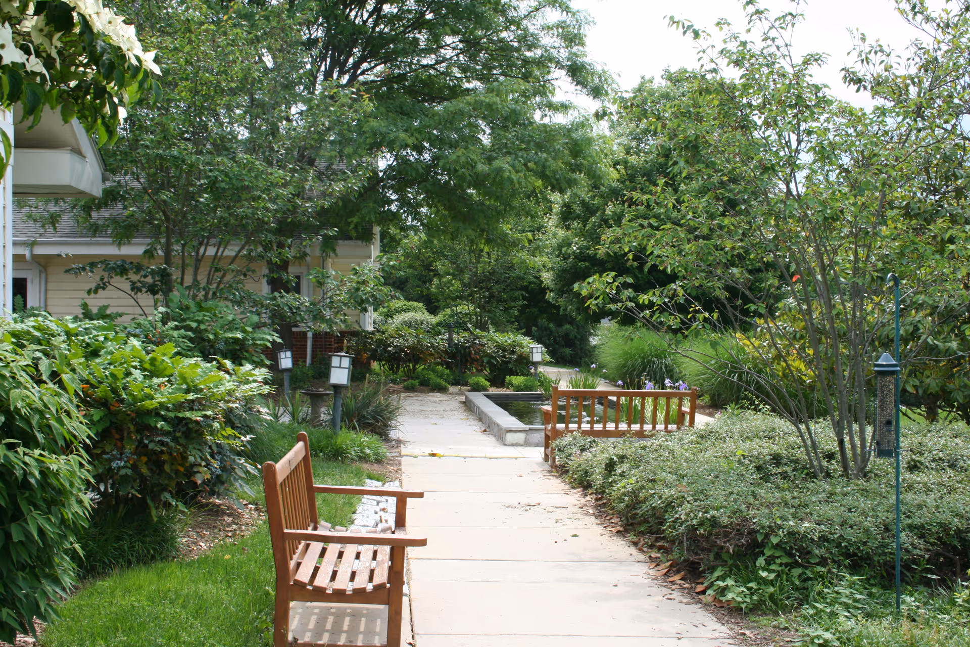 A serene garden path with benches and lush greenery beside a building.
