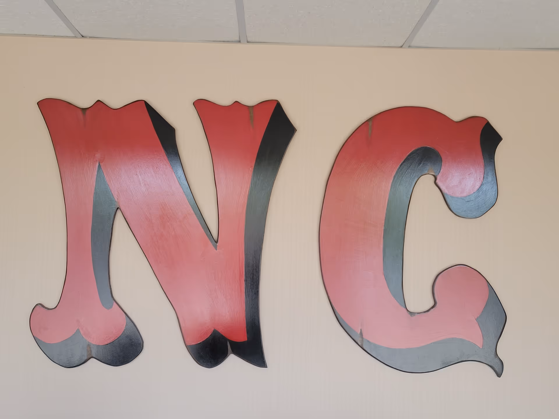 Large pink and gray decorative letters NMC mounted on a beige wall.