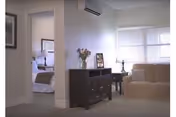 Light-filled living room with sofa, chair, dark dresser, and doorway to a bedroom.