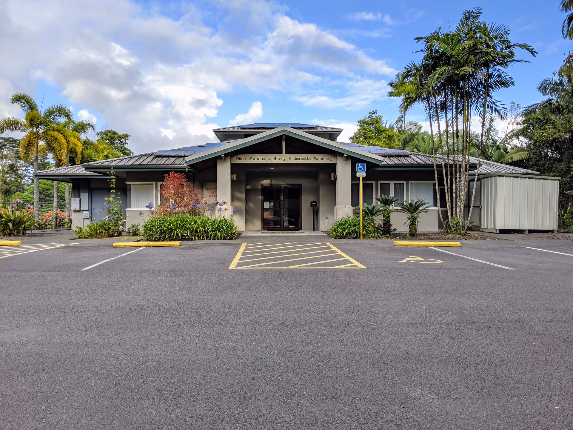 Front view of Hawaiʻi care facility with parking and tropical landscaping.