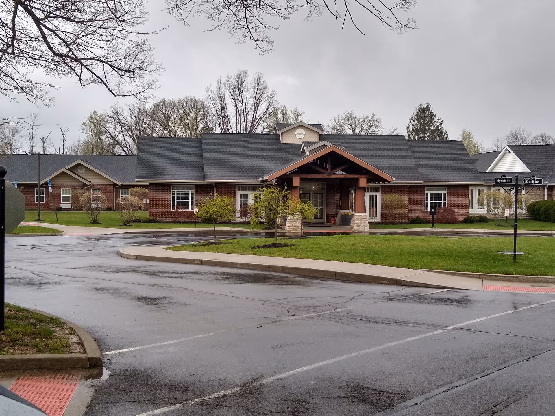 Legacy Village senior living facility exterior, brick building with a covered entrance and manicured lawn.