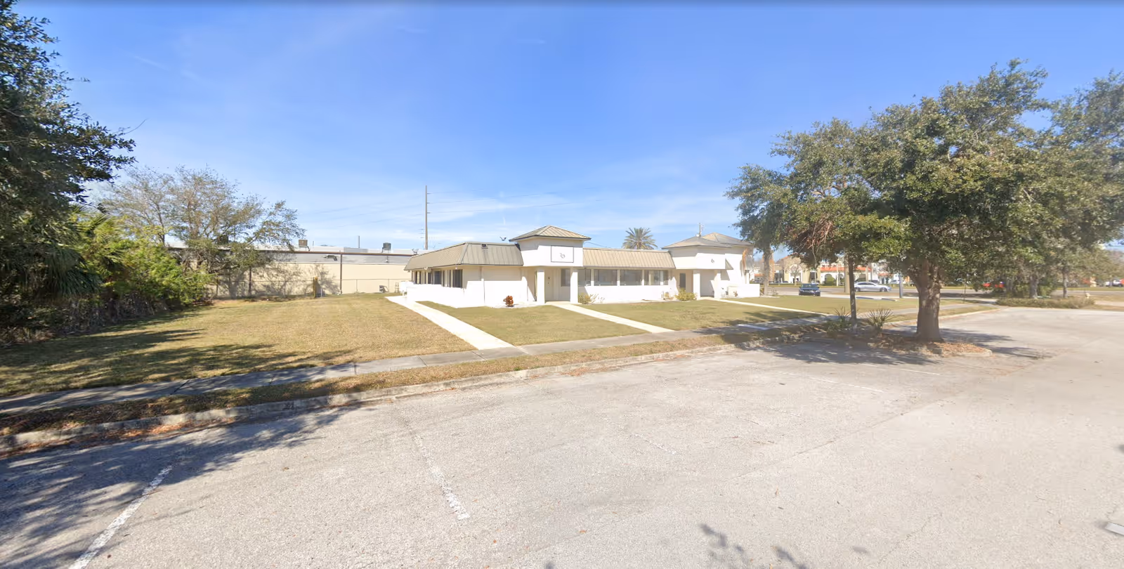 Front exterior of a single-story white building with a lawn, driveway, and trees.
