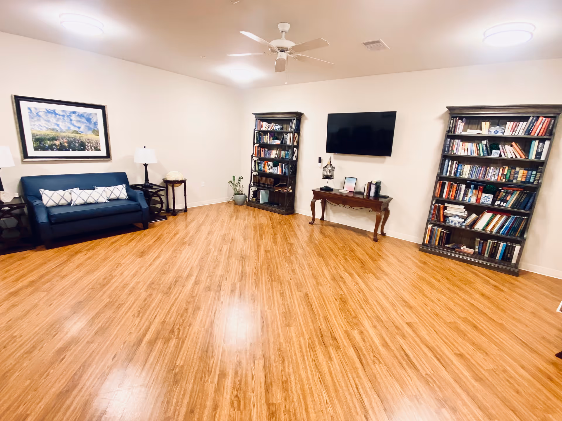 A cozy lounge in a senior living facility with sofa, shelves, and a wall-mounted TV.