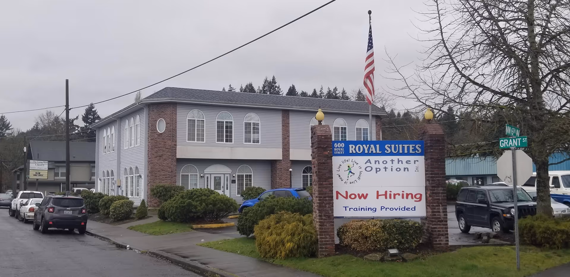 Two-story senior living facility with a large sign and parked cars along the street.