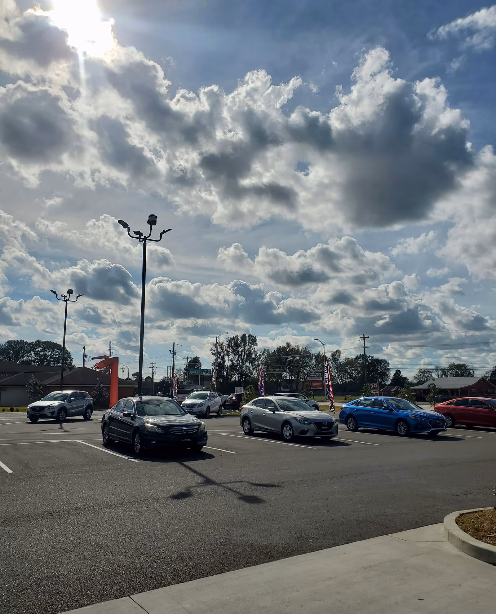 Exterior view of a parking lot with several cars under a cloudy sky.