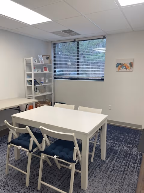 Bright activity room with white tables, chairs, and a windowed wall.