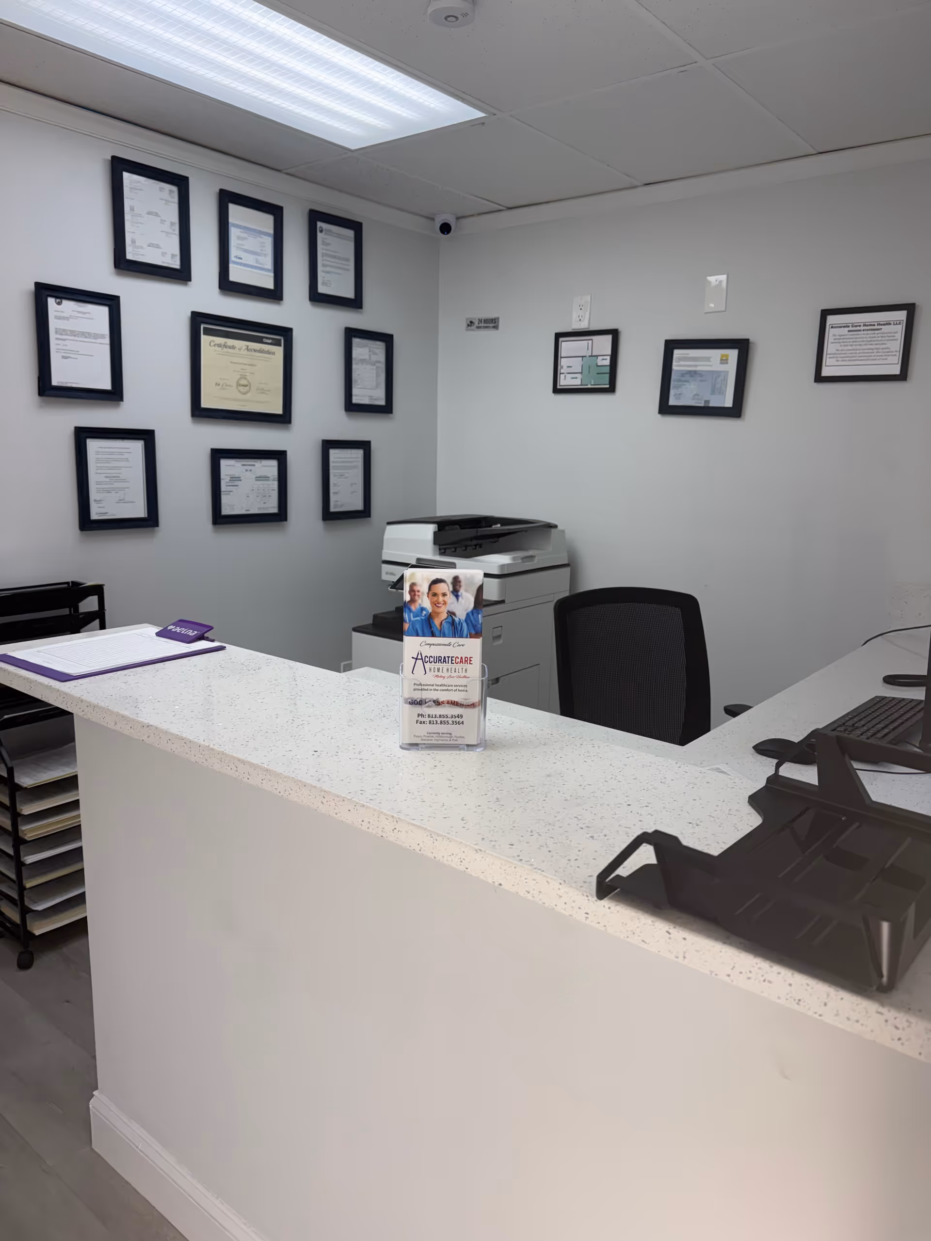 Reception area with white speckled counter, chair, copier, and framed certificates on the wall.