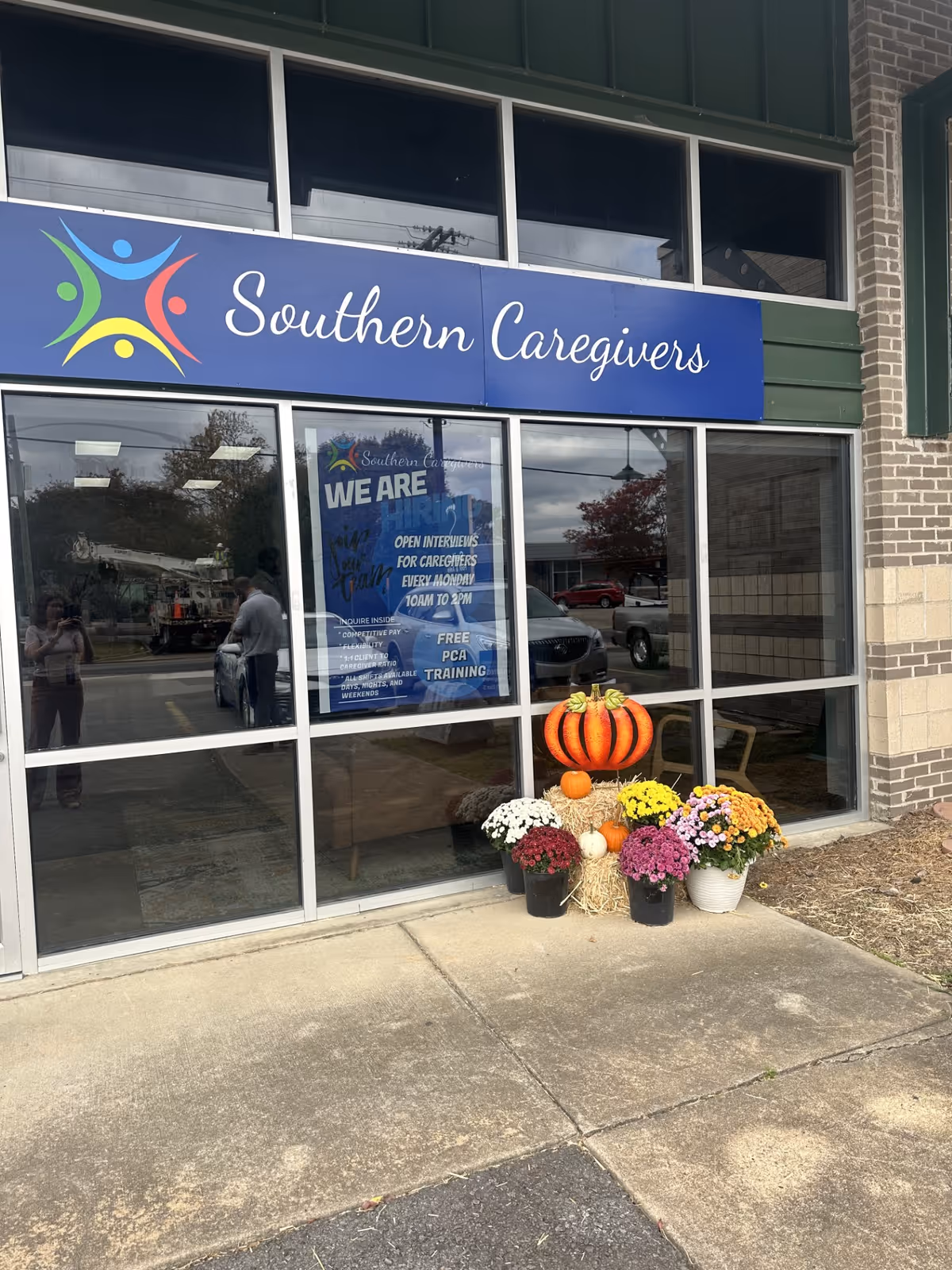 Front of Southern Caregivers facility with blue sign, pumpkins, and potted flowers outside.