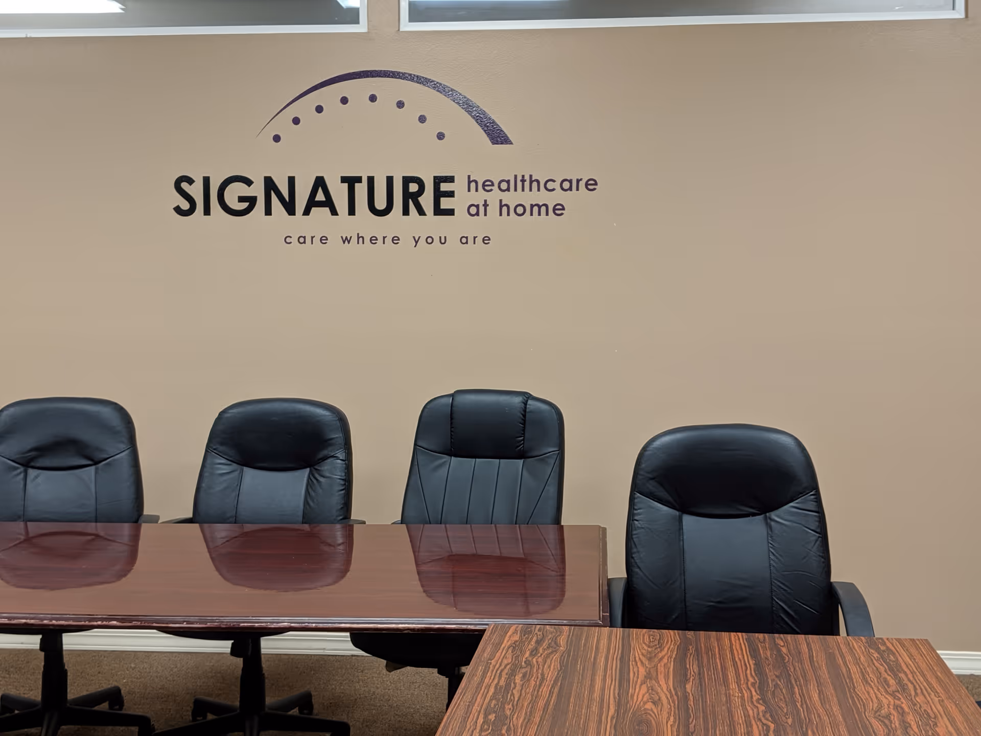 Interior conference room with dark chairs around a polished table under Signature Healthcare at Home logo.