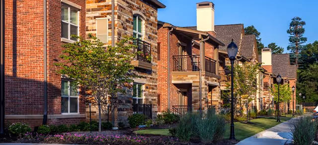 Exterior view of Brookdale Dogwood Creek with brick buildings, trees, and lampposts along a walkway.