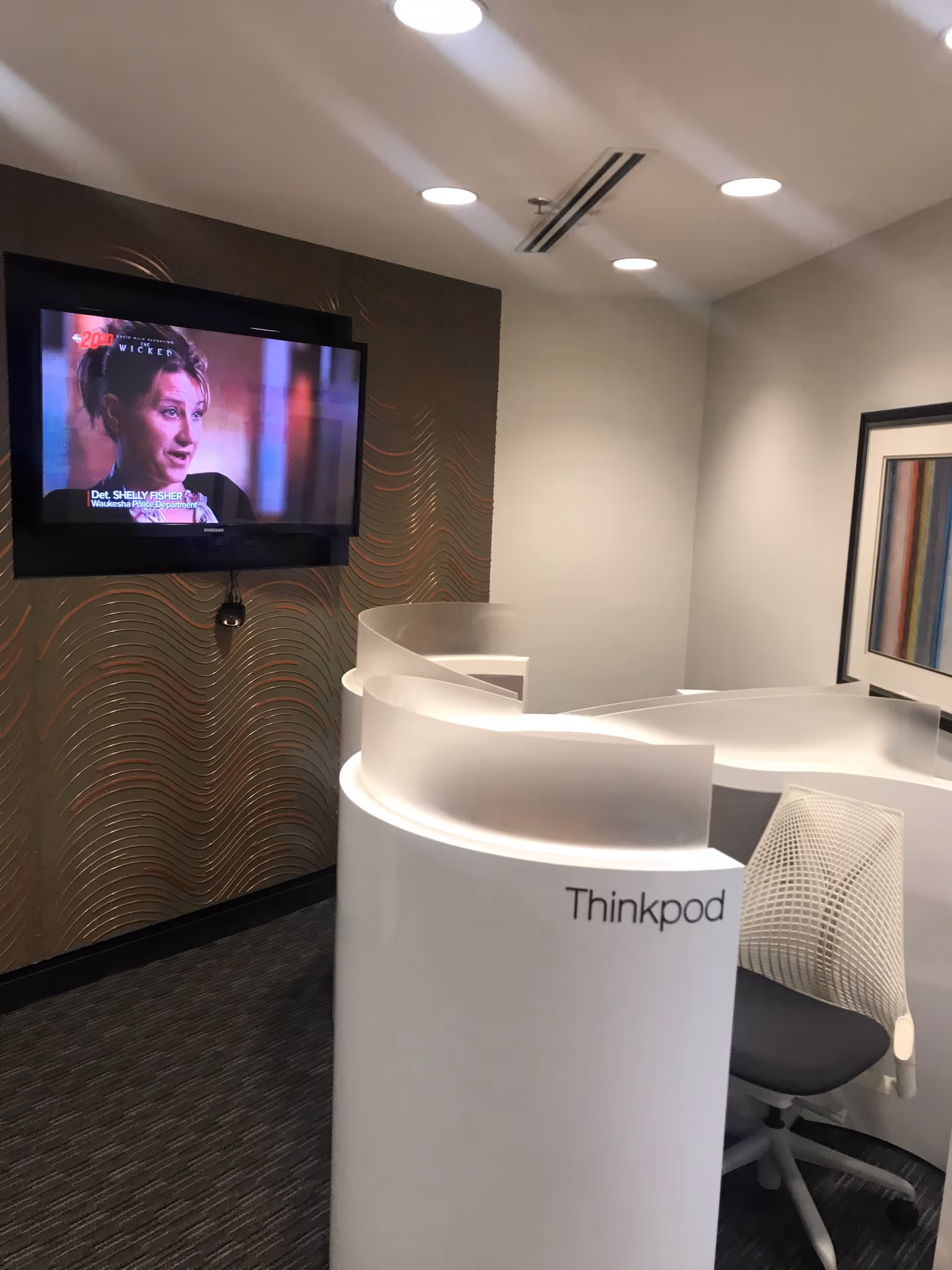 Modern interior featuring a curved Thinkpod reception pod, chair, and wall-mounted TV in a lounge area.